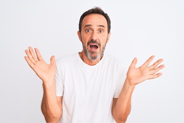 Fototapeta premium Middle age handsome man wearing casual t-shirt standing over isolated white background clueless and confused expression with arms and hands raised. Doubt concept.