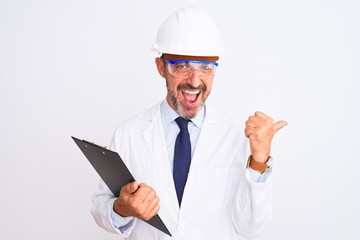 Senior engineer man wearing helmet glasses holding clipboard over isolated white background pointing and showing with thumb up to the side with happy face smiling
