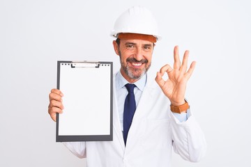 Senior engineer man wearing security helmet holding clipboard over isolated white background doing ok sign with fingers, excellent symbol