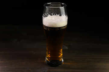 Photo of beer in a glass. Thick foam and a nice color drink on a black background.