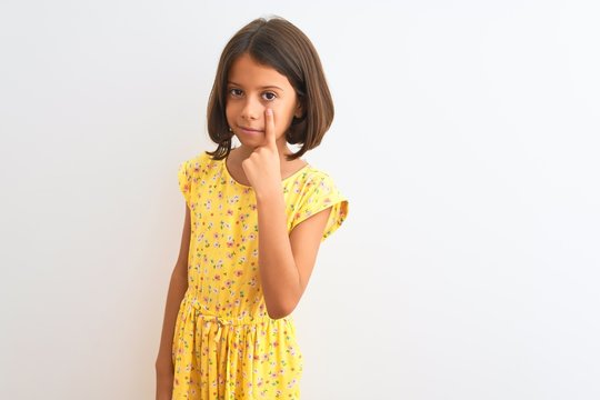 Young beautiful child girl wearing yellow floral dress standing over isolated white background Pointing to the eye watching you gesture, suspicious expression