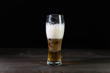 Photo of beer in a glass. Thick foam and a nice color drink on a black background.