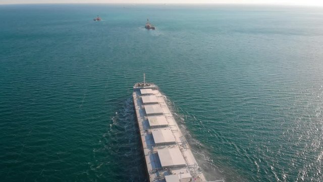 The large cargo vessel left the port after loading and moves in the right direction at high speed. Balker goes in the ocean.