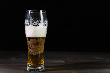 Photo of beer in a glass. Thick foam and a nice color drink on a black background.