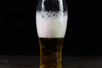 Photo of beer in a glass. Thick foam and a nice color drink on a black background.