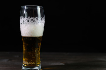 Photo of beer in a glass. Thick foam and a nice color drink on a black background.