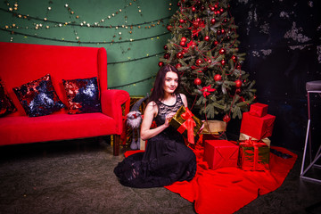 beautiful girl in evening dress with a gift stands near the Christmas tree. copy space 