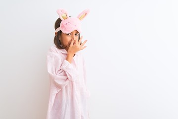 Obraz na płótnie Canvas Beautiful child girl wearing sleep mask and pajama standing over isolated white background smelling something stinky and disgusting, intolerable smell, holding breath with fingers on nose. Bad smell