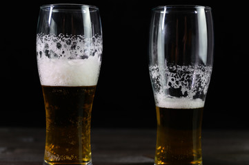 Photo of beer in two glasses. Thick foam and a nice color drink on a black background.