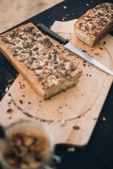 Sliced homemade whole grain bread with pumpkin and sunflower seeds on top. Layed on wooden plate on black backround. Knife in the middle. Selective focus.  L