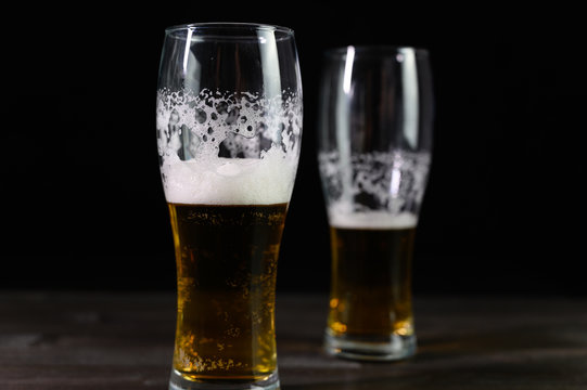 Photo of beer in two glasses. Thick foam and a nice color drink on a black background.