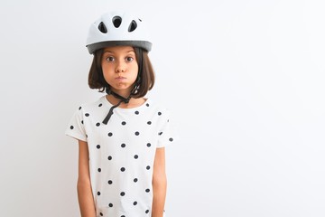 Beautiful child girl wearing security bike helmet standing over isolated white background puffing cheeks with funny face. Mouth inflated with air, crazy expression.