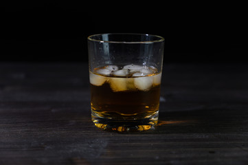 Photo of whiskey in a glass with ice. Real ice and a pleasant color of the drink on a black background.