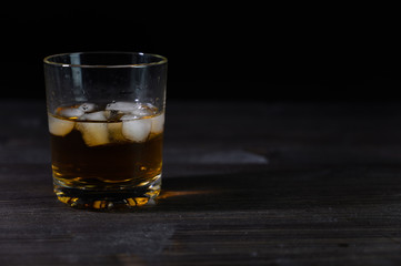 Photo of whiskey in a glass with ice. Real ice and a pleasant color of the drink on a black background.