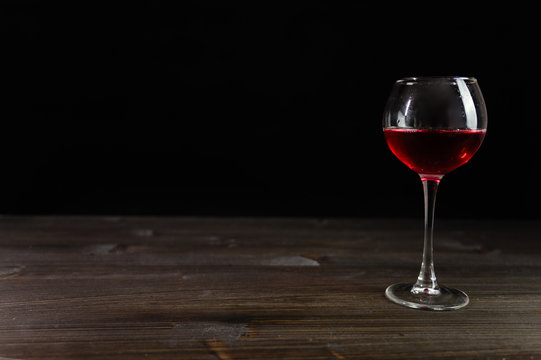 Photo of red wine in a glass on a wooden table. Nice color drink on a black background.