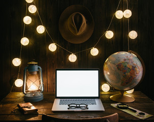 Evening view of traveler's desk with laptop, globe model, gas lamp, wall with hat and electric garland