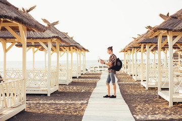 Side view - a young traveler guy with a backpack is looking at a smartphone and is guided around the map in search of a hotel. The concept of online navigators in the smartphone