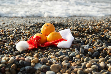 Fototapeta na wymiar Santa Claus hat with tangerines on the beach