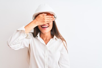 Young beautiful architect woman wearing helmet and glasses over isolated white background smiling and laughing with hand on face covering eyes for surprise. Blind concept.