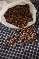 Roasted coffee beans in white paper bag. Beans sprinkled on the table. Coffee on a navy blue checkered background.