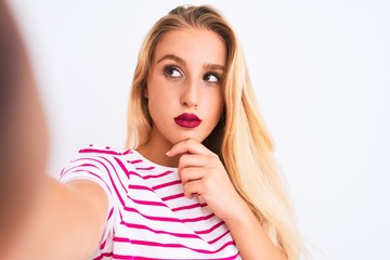 Beautiful woman wearing striped t-shirt make selfie by camera over isolated white background serious face thinking about question, very confused idea