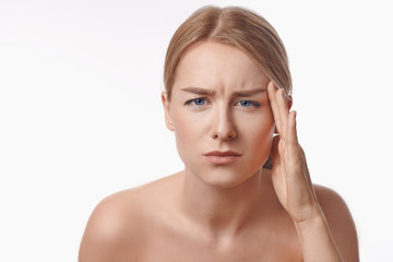 Portrait of a sexy blond caucasian young woman frowning looking in the mirror, observing facial wrinkles, first sign of aging