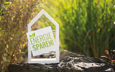 Weißes Haus im Garten mit Schild Energie sparen!