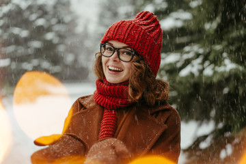 Young beautiful woman in knitted red hat and scarf standing in the park and catching snow