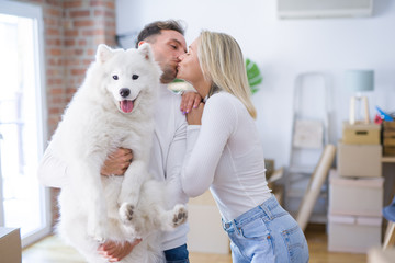 Young beautiful couple with dog kissing standing at new home around cardboard boxes