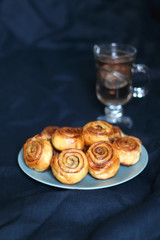 Homemade cinnamon rolls on a plate and cup of tea. Selective focus, dark background.