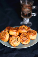 Homemade cinnamon rolls on a plate and cup of tea. Selective focus, dark background.