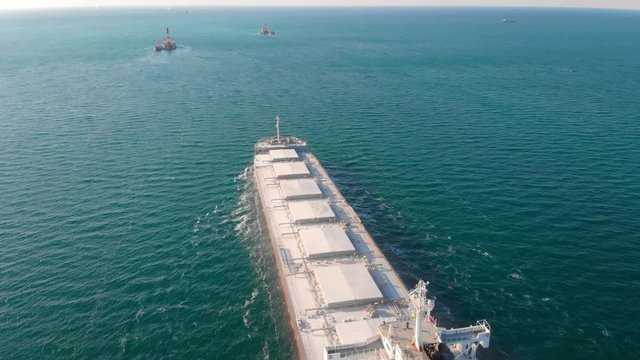 The large cargo vessel left the port after loading and moves in the right direction at high speed. Balker goes in the ocean.