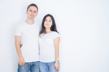 Young beautiful couple wearing casual t-shirt standing over isolated white background with serious expression on face. Simple and natural looking at the camera.