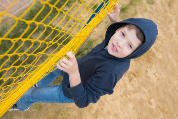 a boy in a blue jumper with a hood, climbs on a yellow grid, up