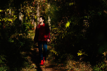 Beautiful young man walking in forest in casual clothes