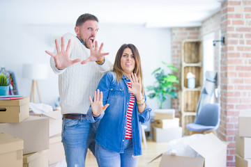 Obraz premium Young beautiful couple standing at new home around cardboard boxes afraid and terrified with fear expression stop gesture with hands, shouting in shock. Panic concept.