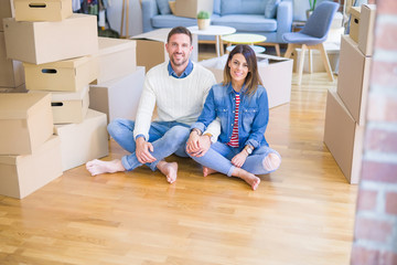 Young beautiful couple sitting on the floor at new home around cardboard boxes