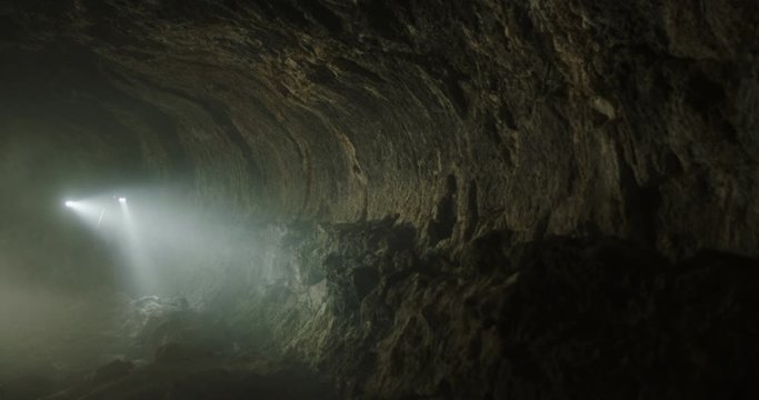 Tracking shot of explorers hiking through smoky cave towards camera