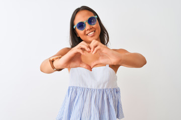 Young chinese woman wearing striped dress and sunglasses over isolated white background smiling in love showing heart symbol and shape with hands. Romantic concept.