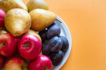 Fresh organic pears, apples, plums on an orange background. Autumn harvest. Free space for text.