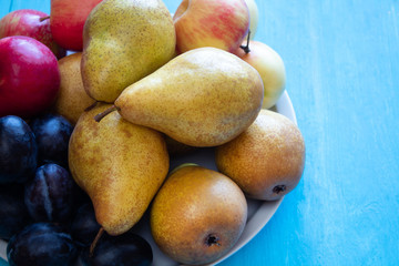 Fresh organic pears, apples, plums on a blue woody background. Autumn fruit harvest