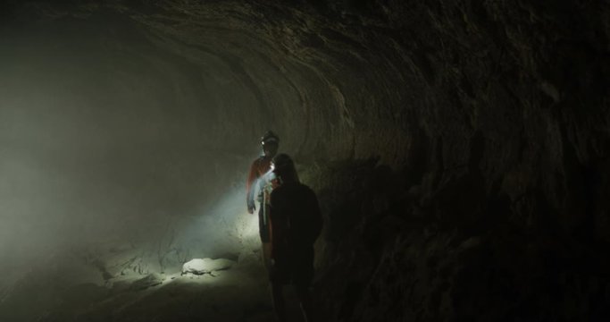 Cavers hiking away from the camera while exploring underground with headlamps
