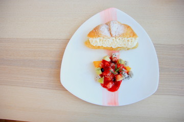 Croissant and cream with  fruit in white discon the wooden table.
