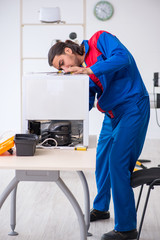 Obraz premium Young male contractor repairing refrigerator at workshop