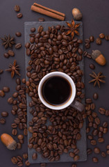 Beautiful composition of coffee beans, utensils for making coffee and decor in the form of almonds, dried slices of lemon, peanut and cinnamon on black and blue backgrounds.