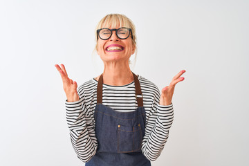 Middle age chef woman wearing apron and glasses over isolated white background celebrating mad and crazy for success with arms raised and closed eyes screaming excited. Winner concept
