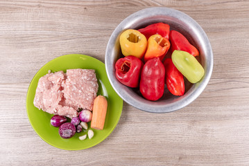 Ingredients for stuffing peppers, minced pork, onions, garlic, carrots laid out on a green plate and peeled peppers in an aluminum basin
