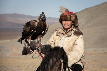 Portrait of a traditional kazakh eagle hunter with his golden eagle on horseback. Ulgii, Mongolia.