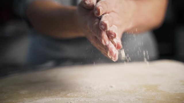 Close up, slow motion view of woman's hands wiping off flour after working with pastry dough. Lady wipes hands together as dough and flour falls to the counter.