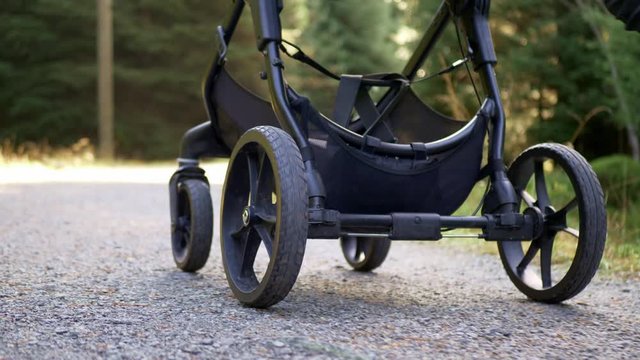 Young female pushing baby pram in woodland wilderness outdoors. Focus low angle on pram wheels.